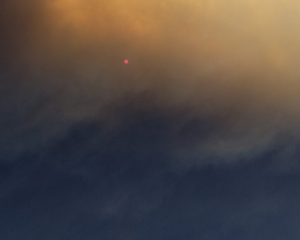 A mix of yellow and dark blue smoke in front of a small, bright red sun